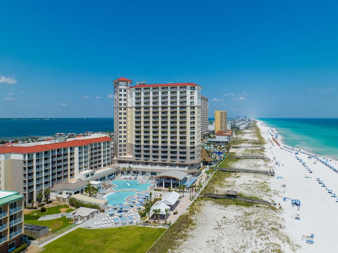 Photo of Hilton Pensacola Beach Gulf Front Hotel, a multi-story hotel beside a white sand beach and green-blue ocean water.